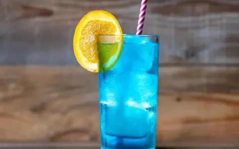 Orzeźwiający drink z blue curacao, ozdobiony plasterkiem pomarańczy i limonki, z kolorową słomką. Idealny na letnie popołudnie.
