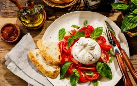Pyszna burrata z pomidorami i bazylią, podana z chrupiącym pieczywem. To jest właśnie burrata – ser, który rozpływa się w ustach!