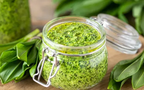 Słoik pełen aromatycznego pesto z czosnku niedźwiedziego, otoczony świeżymi liśćmi tej wiosennej rośliny.