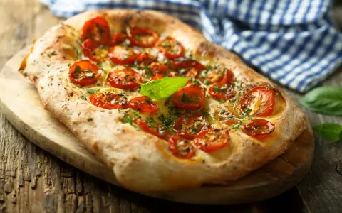 Pyszna focaccia z pomidorkami koktajlowymi i bazylią. Idealna jako przekąska lub dodatek do dania. Z czym jeść? Z sałatką, dipem lub solo!