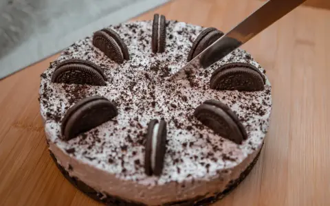 Pyszny sernik oreo, ozdobiony ciasteczkami i posypką, czeka na pokrojenie.