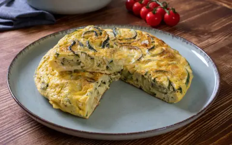 Pyszna frittata z cukinią, podana na talerzu, z pomidorkami koktajlowymi w tle.
