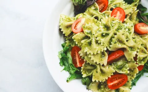 Makaron farfalle z zielonym pesto ze słoika, udekorowany połówkami pomidorków koktajlowych i listkami sałaty.