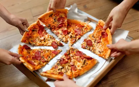 Ręce sięgają po kawałki pysznego ciasta na pizzę z kiełbasą i grzybami.
