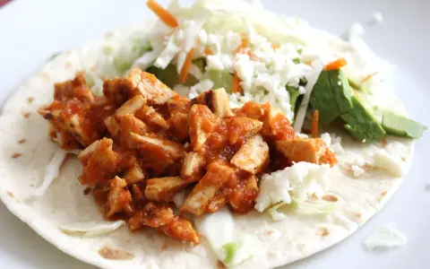 Pyszna tortilla z kurczakiem w sosie, posypana serem feta, z dodatkiem świeżej sałaty i awokado.