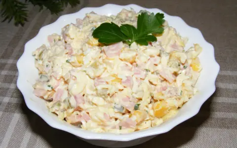 Pyszna sałatka z szynką, jajkiem, kukurydzą i ogórkiem, udekorowana natką pietruszki. Idealna na każdą okazję.