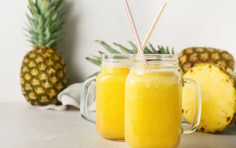 Orzeźwiający drink w ananasie, podany w słoikach, z kawałkami ananasa w tle.