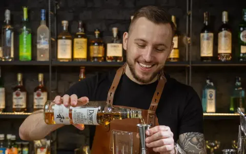 Uśmiechnięty barman, który robi drinki, nalewa whisky Dewar's do jiggera.