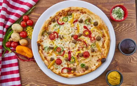 Pizza z mięsem mielonym, papryką, cebulą i kukurydzą. Obok sosy i warzywa, co zamiast śmietany?