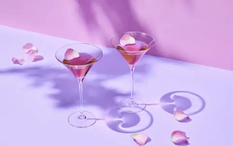 Dwa różowe drinki w kieliszkach do martini, ozdobione płatkami róż. Idealne co do martini na romantyczny wieczór.