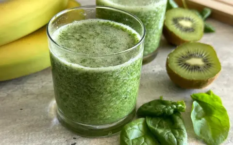 Orzeźwiający koktajl ze szpinakiem, bananami i kiwi. Zielony napój w szklance, obok świeże liście szpinaku i owoce.