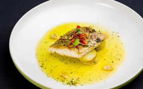 Filet ryby w aromatycznym sosie cytrynowym, podany na plastrach ziemniaków.