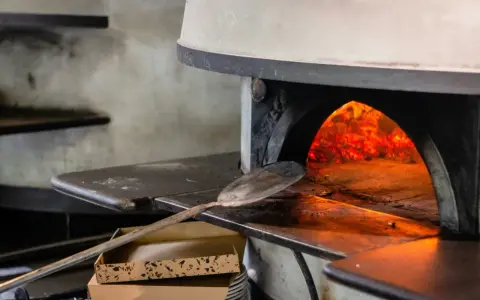 Piec do pizzy z rozżarzonymi węglami. Łopatka czeka, by włożyć do środka pizzę, która będzie piec się w 200 stopniach.