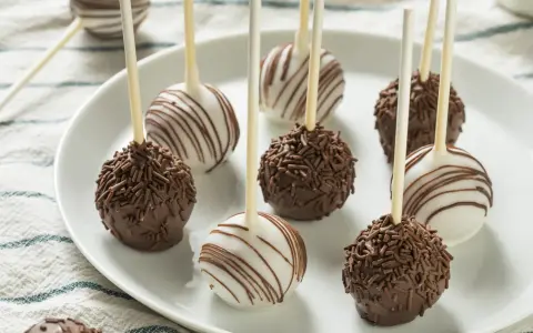 Pyszne cake pops przepis na talerzu: czekoladowe z posypką i białe z polewą.