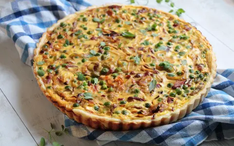 Pyszna tarta z porem i boczkiem, udekorowana groszkiem i ziołami, na niebiesko-białej kratce.