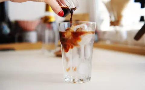 Ręka wylewa espresso na lód w szklance. Idealny napój na upalne dni - tonic espresso.