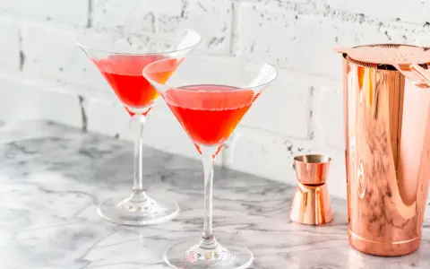 Dwa kieliszki z czerwonym drinkiem, idealne na letnie wieczory. W tle miedziany shaker i miarka, sugerujące przygotowanie drinka bacardi ze spritem.