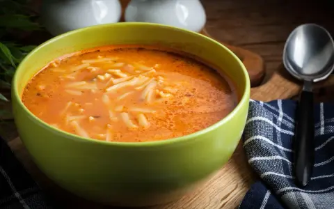 Miseczka pomidorowej z makaronem, idealna jako co do zupy zamiast śmietany. Obok łyżka i serwetka.