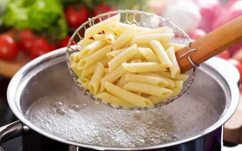 Penne makaron w cedzaku nad garnkiem z wrzącą wodą. Czas, ile się gotuje makaron, zależy od jego rodzaju.