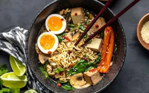 Miseczka ramenu z makaronem, jajkiem na pół, tofu, grzybami i szpinakiem. Dodatki do ramenu tworzą apetyczną całość.