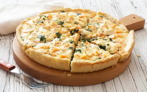 Pyszna tarta z łososiem, szpinakiem i serem feta, pokrojona na kawałki, czeka na talerzu.