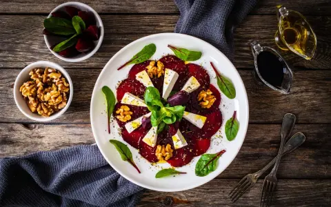 Eleganckie carpaccio z buraka z serem feta, orzechami włoskimi i świeżymi ziołami, podane na białym talerzu.
