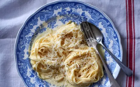 Pyszny makaron alfredo przepis na talerzu z widelcem i łyżką, posypany startym parmezanem.