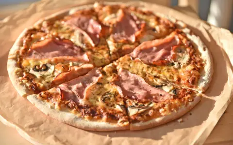 Pizza z szynką i pieczarkami do pizzy, pachnąca i apetyczna, gotowa do podania.