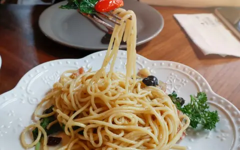 Widok z bliska na talerz pysznego spaghetti aglio e olio, z widelcem unoszącym porcję makaronu, pomidorkiem i bazylią.