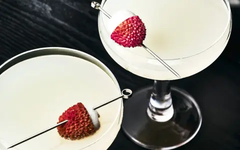 Dwa eleganckie drinki z liczi, ozdobione owocami na patyczkach, kuszą swoim orzeźwiającym wyglądem.