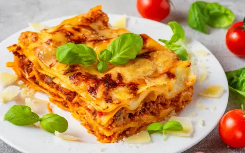 Pyszna, domowa lasagne jak z pieca, z warstwami makaronu, mięsa i sera, ozdobiona świeżą bazylią i parmezanem.