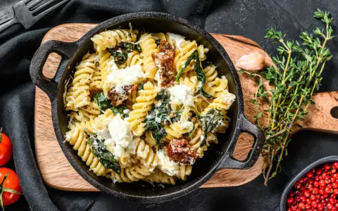 Pyszne fusilli ze szpinakiem i suszonymi pomidorami, posypane parmezanem i kawałkami sera feta.