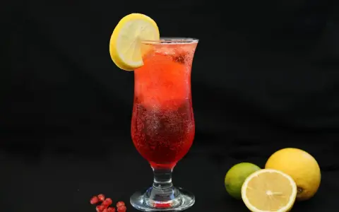 Orzeźwiający drink z granatem, ozdobiony plasterkiem cytryny. Obok leżą świeże owoce: cytryna i limonka.