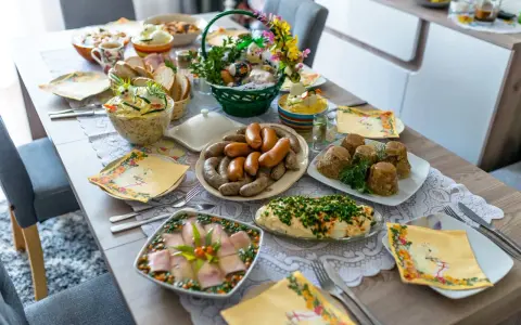 Obficie zastawiony stół z wieloma przystawkami na Wielkanoc: kiełbasy, galarety, sałatki, jajka i koszyczek z ozdobami.