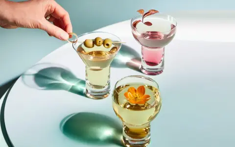 Eleganckie drinki z wódką: martini z oliwkami, różowy koktajl i złoty napój z kwiatem.