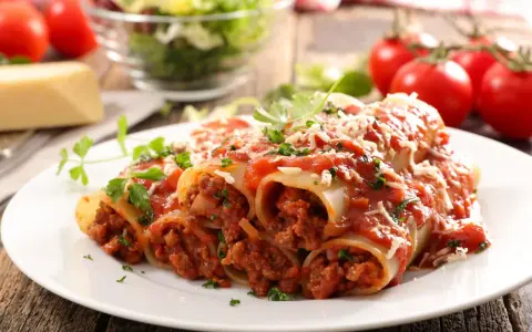 Pyszne cannelloni z mięsem mielonym, polane sosem pomidorowym i posypane parmezanem, na talerzu z pomidorami i sałatką.