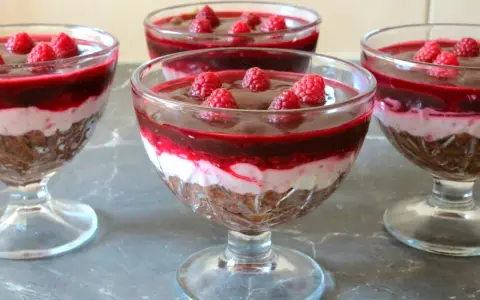 Mini deserki z mascarpone, przełożone warstwą musu i malinową galaretką, ozdobione świeżymi malinami.