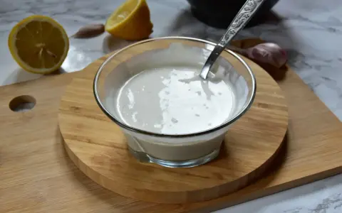 Kremowy sos aioli w szklanej miseczce, obok cytryny i czosnku. Idealny dodatek do dań.