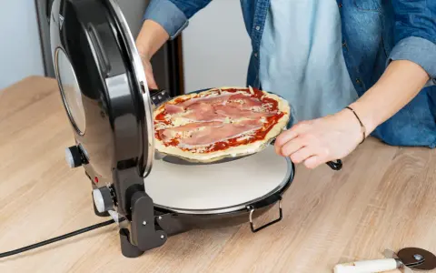 Osoba wkłada pizzę z szynką do okrągłego piekarnika. Idealny moment na pieczenie pizzy w piekarniku!