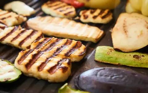 Grillowany ser halloumi z paskami od rusztu, obok cukinia, bakłażan i inne warzywa.