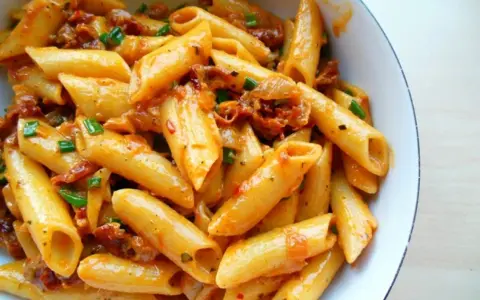 Penne z sosem z suszonych pomidorów i zieloną cebulką, apetyczne danie pełne smaku.