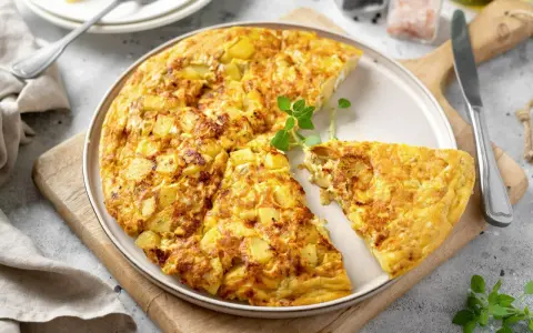 Złocista frittata z ziemniakami, pokrojona na kawałki, podana na talerzu z gałązką ziół.