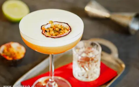 Pyszny drink Pornstar Martini z pianką i owocem marakui, obok kieliszek z drinkiem i połówka limonki.