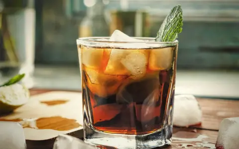 Orzeźwiający gin z colą, z lodem i listkiem mięty, na drewnianym blacie. Idealny na letnie popołudnie.