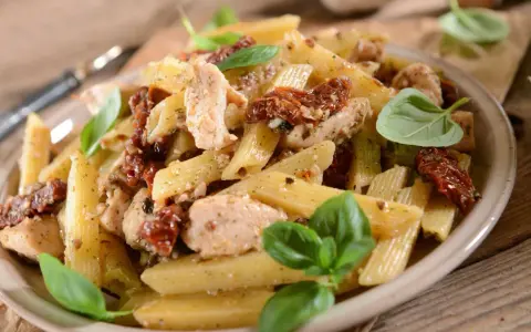 Penne z kurczakiem i suszonymi pomidorami, udekorowane świeżą bazylią. Pyszne danie na obiad.