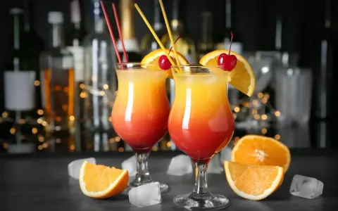 Dwa drinki z wódką, ozdobione pomarańczą i wiśnią, na tle barowych butelek. Idealne na letnie wieczory.