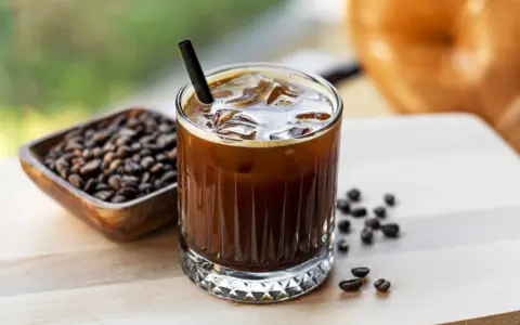 Orzeźwiający cold brew z lodem i słomką, obok miseczka z ziarnami kawy. Idealny na gorący dzień.