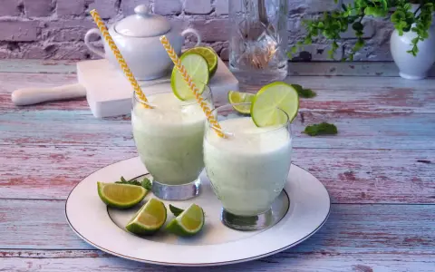 Dwa orzeźwiające drinki z mlekiem skondensowanym, ozdobione plasterkami limonki i miętą, na talerzu.