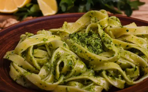 Pappardelle z aromatycznym makaronem z pesto, podane na glinianym talerzu. W tle cytryny i rukola.