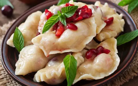 Pyszne, domowe ciasto na pierogi z wiśniami i miętą, podane na glinianym talerzu.